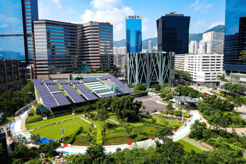 Fotografía de ciudad moderna con zonas verdes, edificios con paneles solares, rodeado de rascacielos